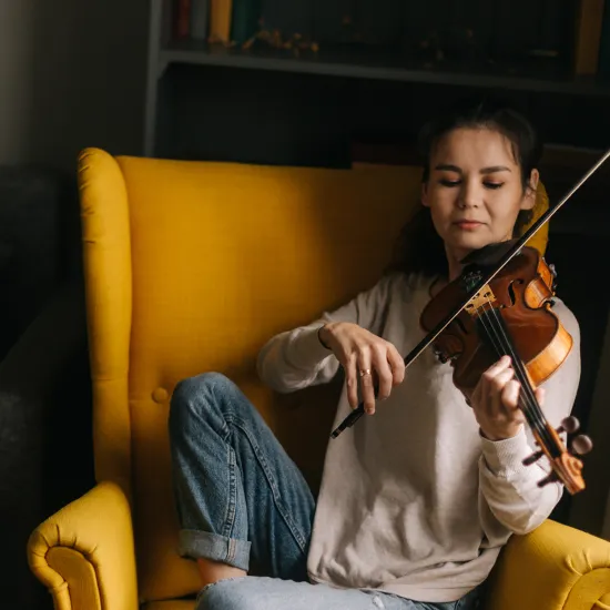 Lady sitting in a yellow chair playing the violin