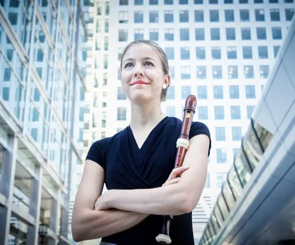 Person in a black shirt holds a recorder, standing in an urban setting with modern glass buildings in the background.