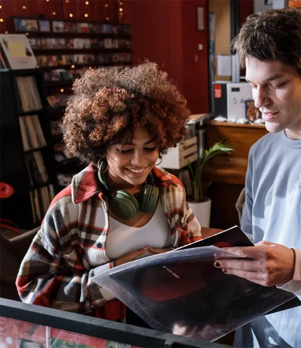 Two people in a record store look at an album cover together. The store has shelves filled with vinyl records.