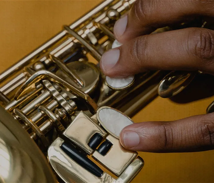 Close-up of a person's hands playing a saxophone, focusing on their fingers pressing the instrument's keys.