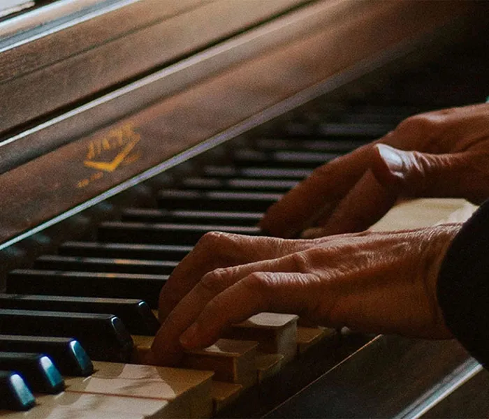 Close-up of hands playing a piano keyboard, showing the pianist's fingers on the keys with a focus on the rich, wooden surface of the piano.