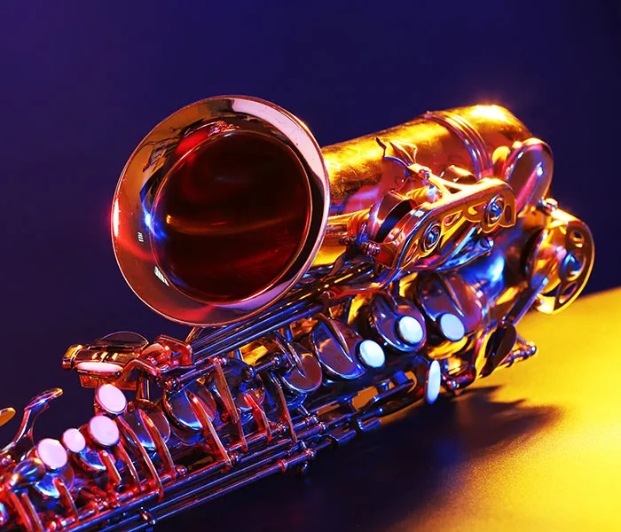 Close-up shot of a shiny saxophone reflecting colorful lights, placed on a dark surface against a gradient blue background.