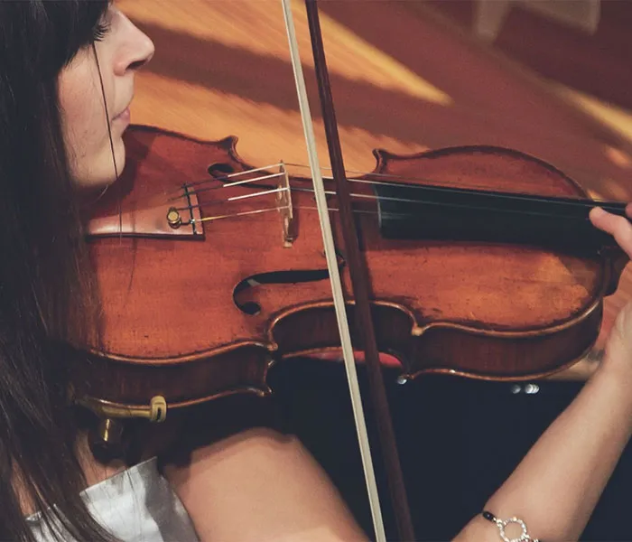 Close-up of a person playing a violin with a bow, focusing on the instrument and the right hand holding the bow.