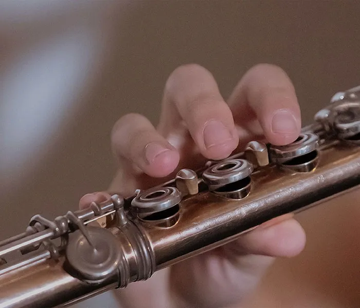 Close-up of a person's hand playing a silver flute, with fingers pressing down on the keys.