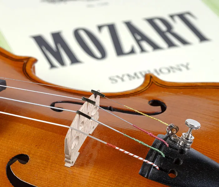 Close-up of a violin placed on sheet music for a Mozart symphony, focusing on the bridge and strings of the instrument.