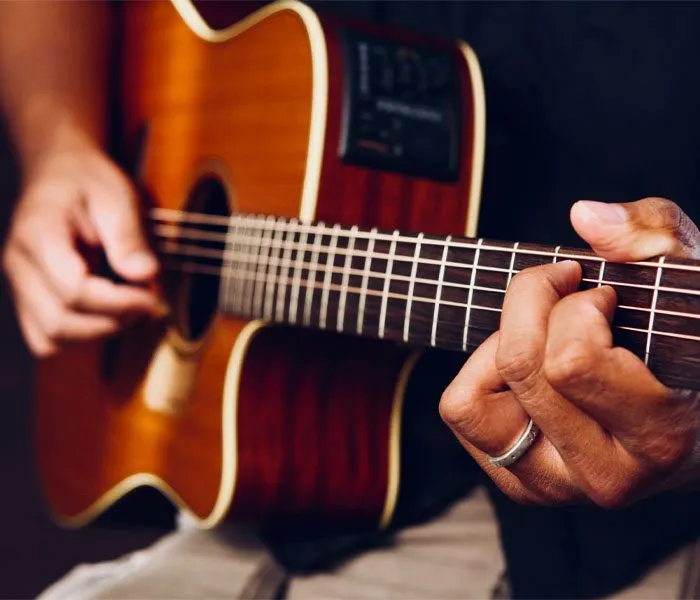 Close-up of a person playing an acoustic guitar, focusing on their hands strumming and fretting the strings.