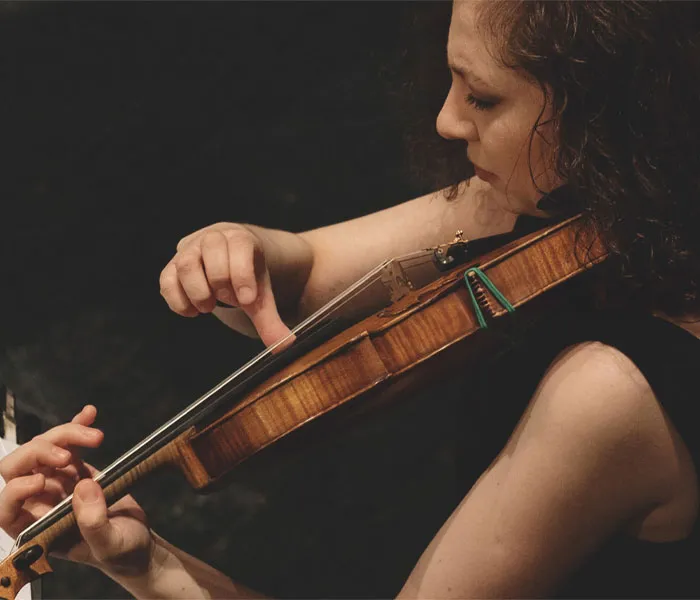 A person with curly hair plays a violin, focusing intently on their finger placement and the instrument's strings.