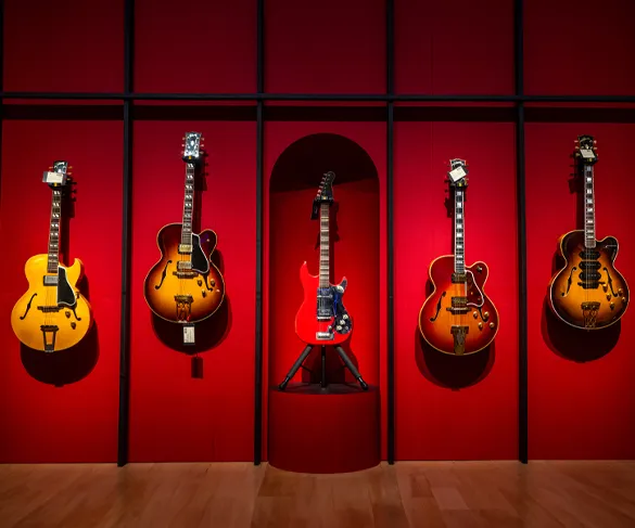 A display of five guitars is mounted on a red wall, with the central guitar in a red alcove and four others on either side.