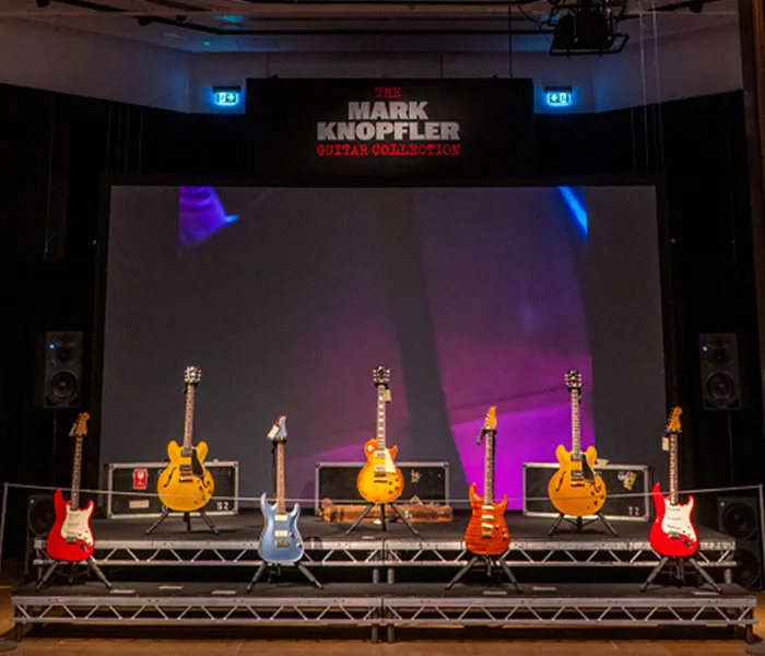 A display setup featuring an assortment of guitars on stands with a sign above that reads 