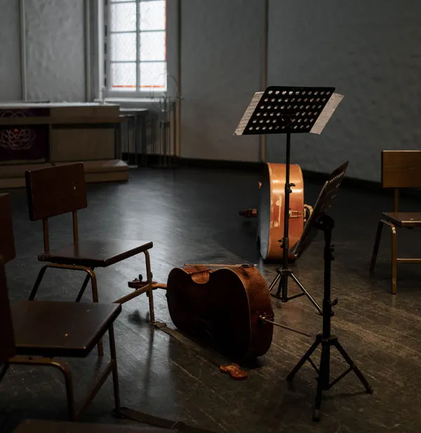 A music room with empty chairs, a music stand, and a cello placed on the floor.