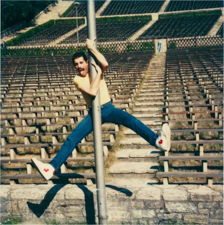 Person in casual attire hangs from a pole with legs spread out wide in an empty outdoor stadium.