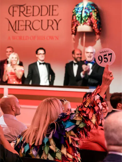 A person holds up bid paddle 957 at an auction. The screen displays 