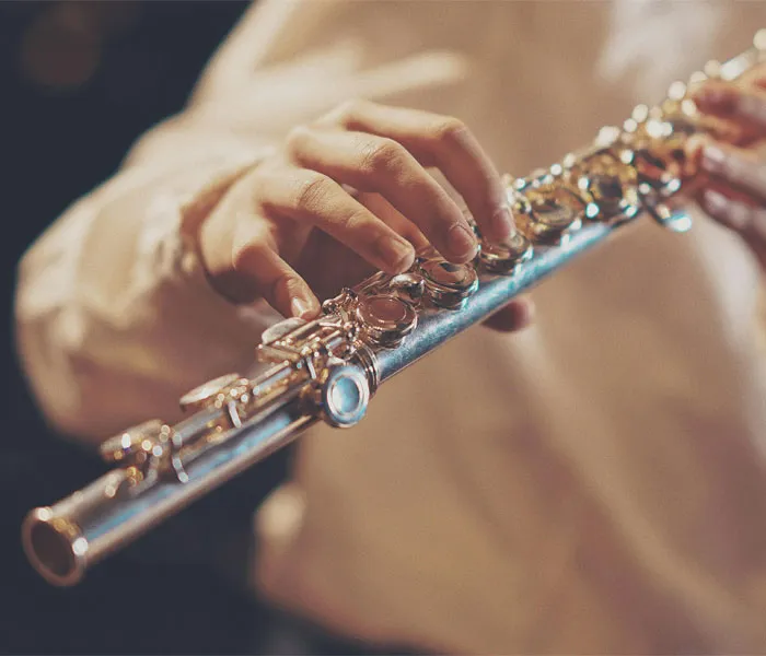 Close-up of hands playing a silver flute, focusing on fingers pressing the instrument's keys.